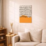 北欧ミニマルなリビング空間に飾られたブラックラインとオレンジの抽象アート（A3サイズ相当）。