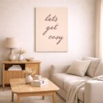 北欧ミニマルなリビング空間に飾られた「Let’s Get Cozy」のタイポグラフィアート（A3サイズ相当）